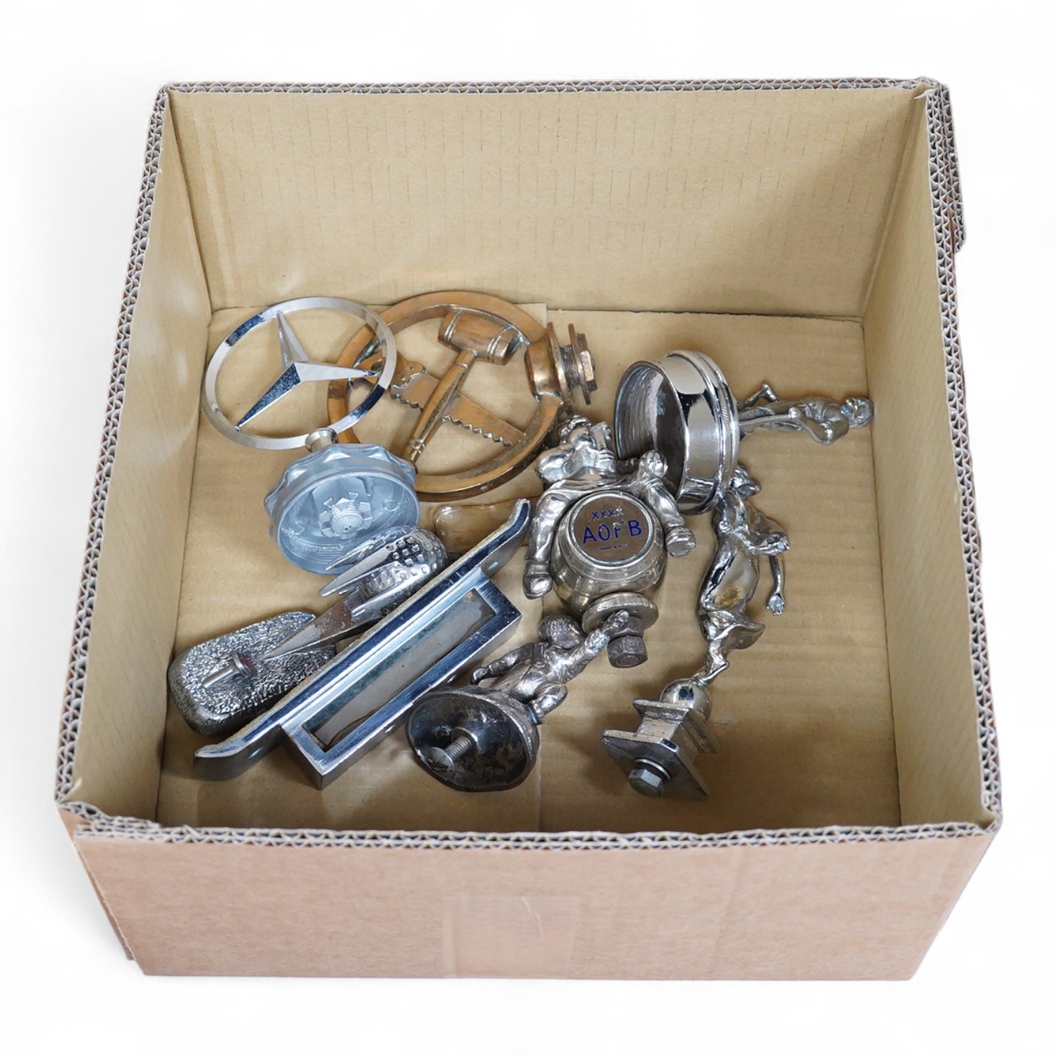 Seven chrome and brass car mascots, including a Mercedes-Benz logo, a figure of a blacksmith, a caricature figure on a beer barrel, a golf ball in mid flight, etc. together with a chromed housing unit for an electric lam